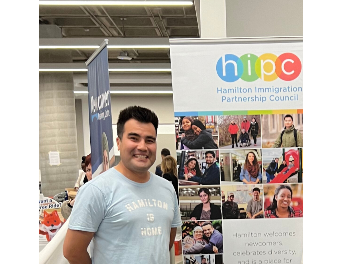 Mohammad Araf poses with a Hamilton Immigration Partnership Council poster.