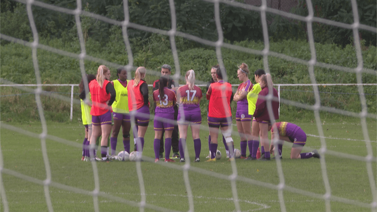 A group of female soccer players at Clapton Community FC, weaing a purple, yellow and red kit form a circle before a game in London, England on November 5, 2023.