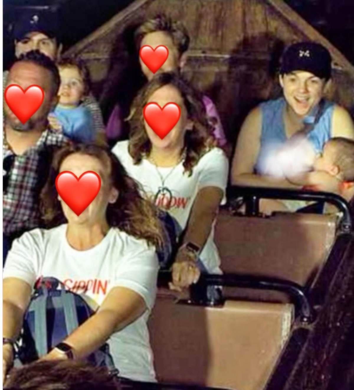 A woman wearing a ballcap is seen breastfeeding her baby in what appears to be a log ride boat. Her breast is blurred. The faces of the other riders are hidden by red heart emojis.