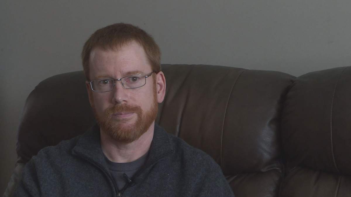 A man with red hair and a beard sits on a couch