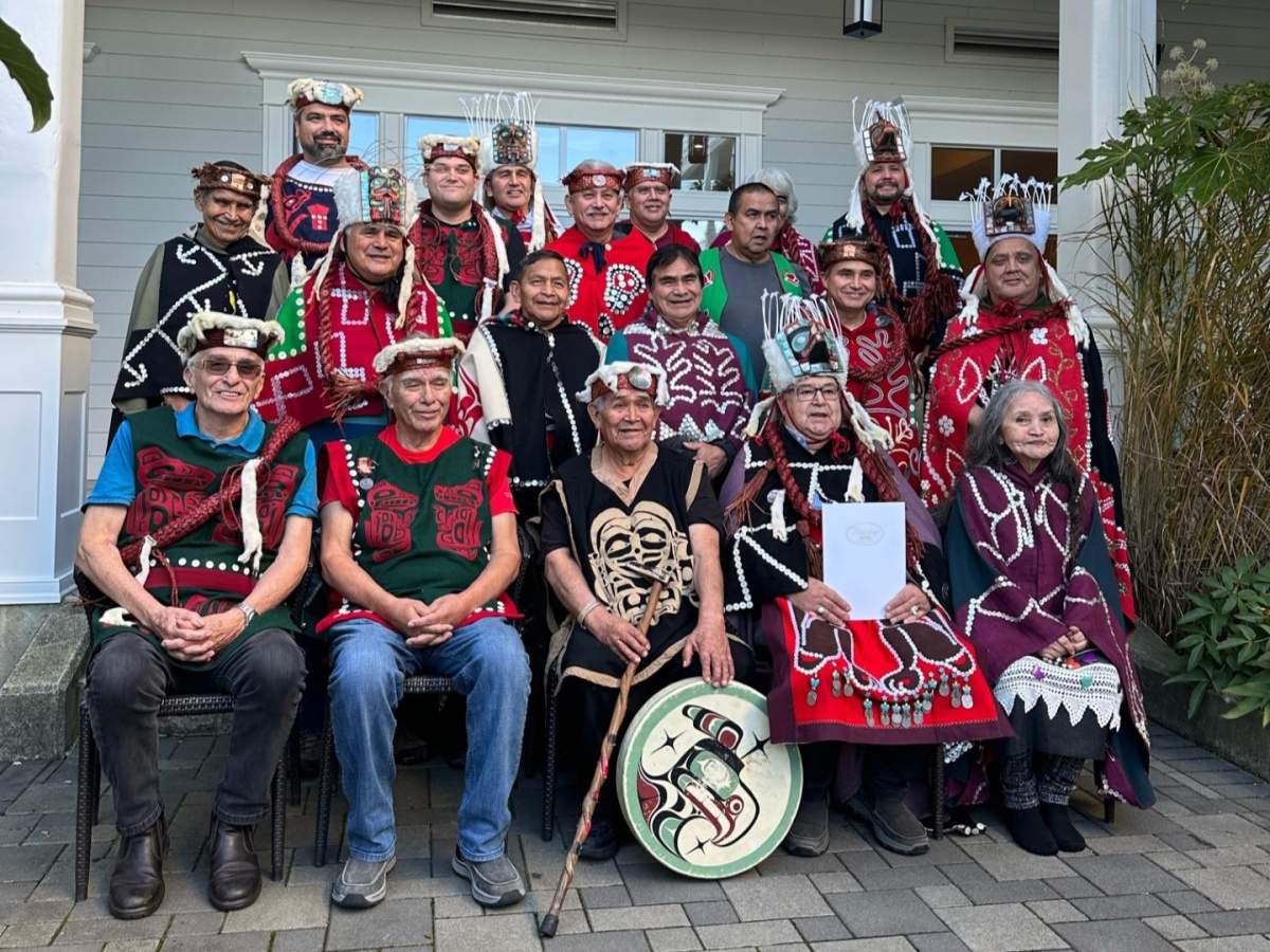 A group of people in traditional regalia are shown posing for a photo.