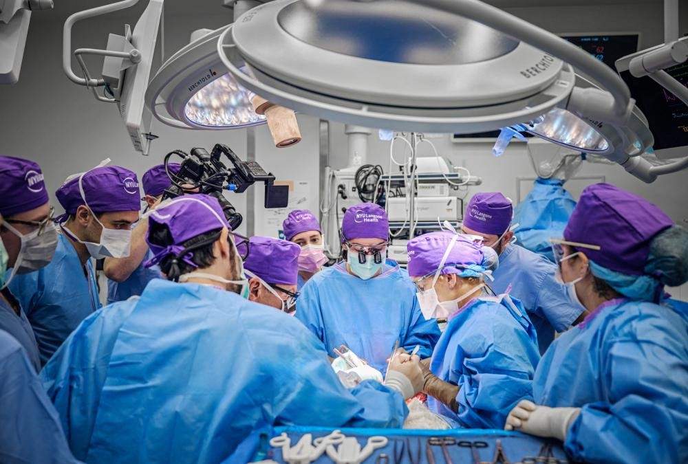 People in blue scrubs and medical gear surround a patient on an operating table.