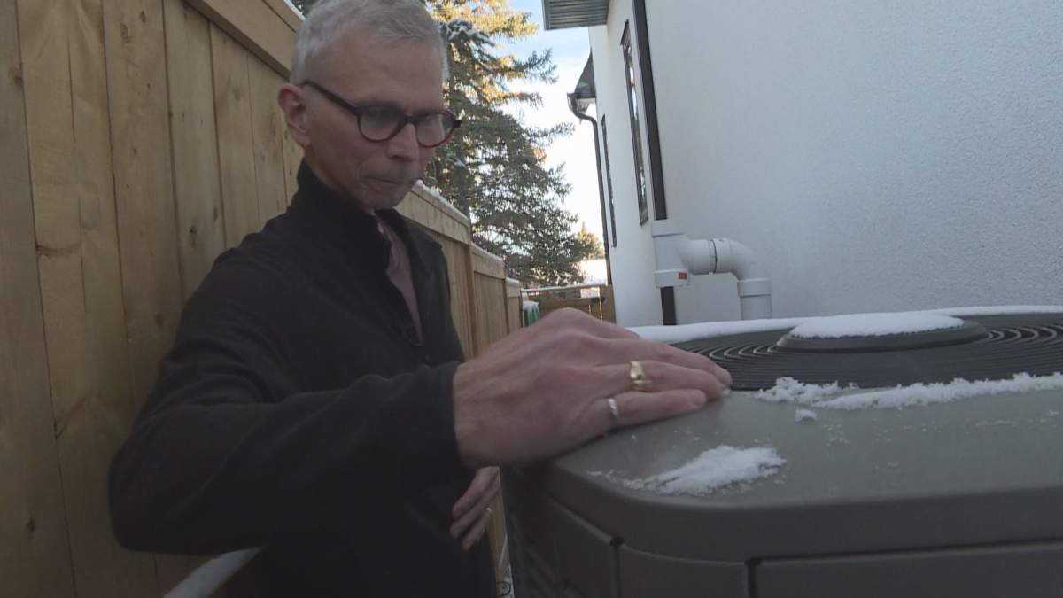 Kirk Bailey removes snow from the top of his recently installed heat pump in Calgary, Alberta.