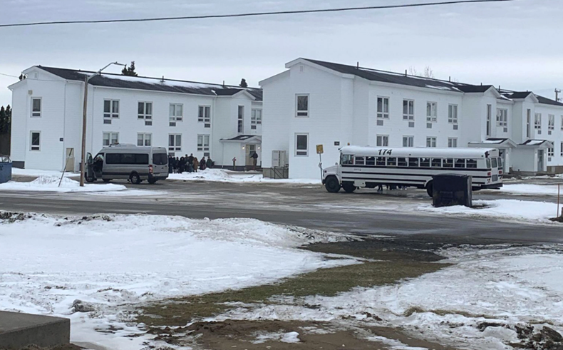 Busses and seen outside two white buildings.