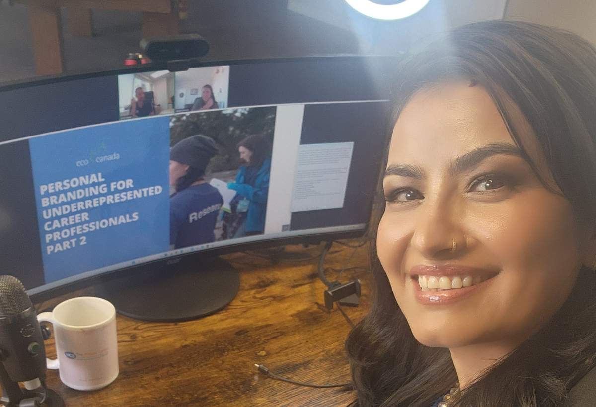 A young woman takes a selfie in front of a computer screen.