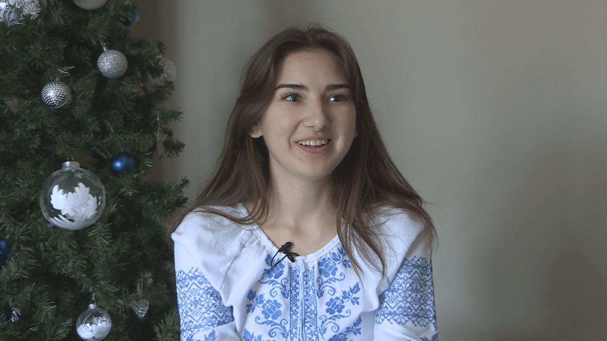 A woman in a blue and white shirt in front of a Christmas tree.