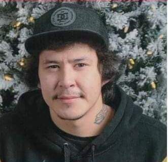 A man poses for a photo a tattoo is visible on the left side of his neck.