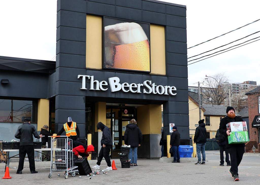 People line up in a parking lot for a long wait to return empties or buy beer at a Beer Store in downtown Toronto