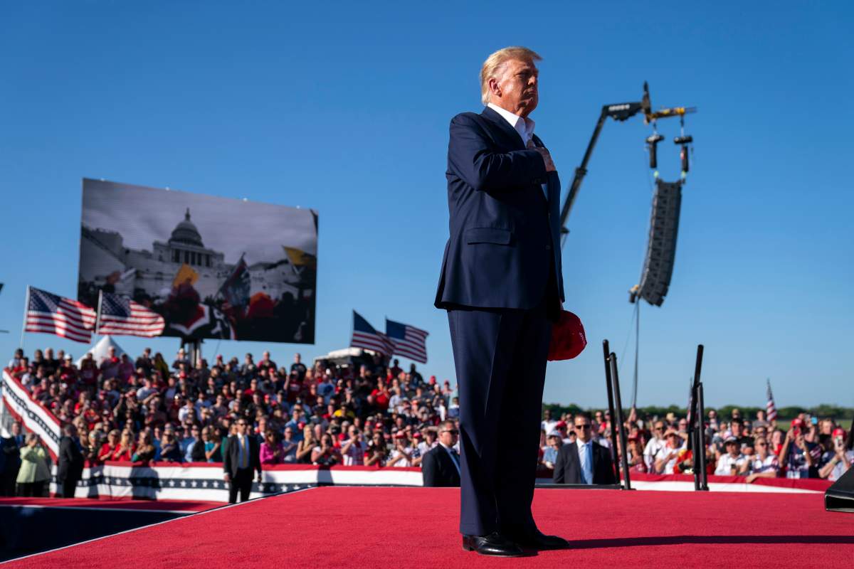 Footage from the Jan. 6, 2021, insurrection at the U.S. Capitol is displayed as former President Donald Trump stands with hand over heart. (AP Photo/Evan Vucci)