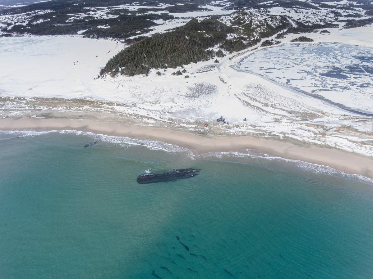 The wreckage can be seen in icy-cold blue water with a shoreline blanketed in snow.