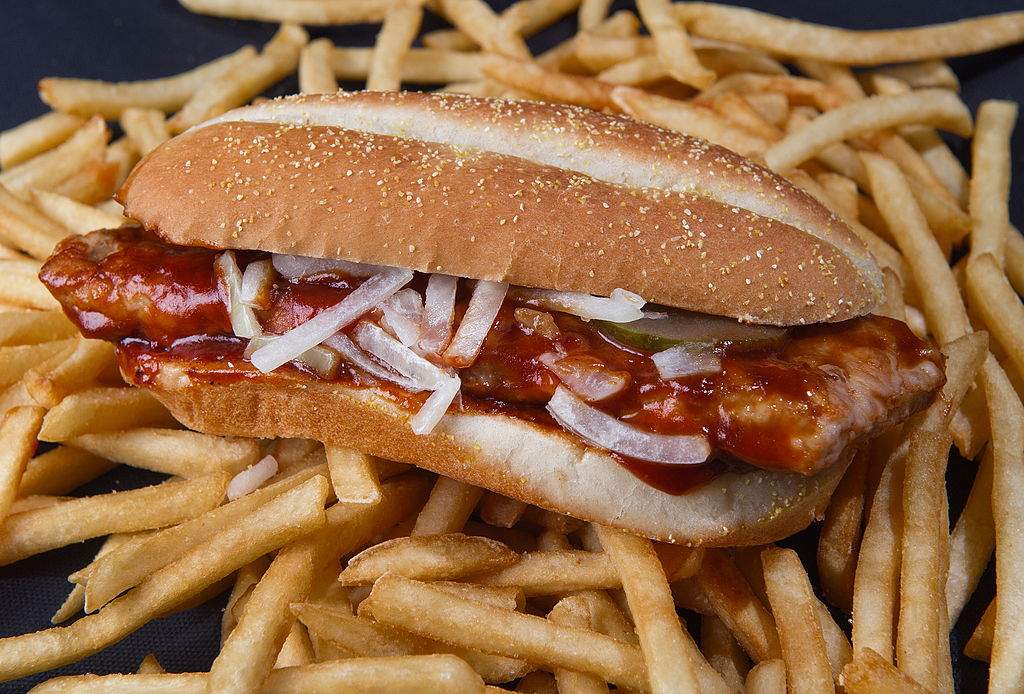 The McRib is pictured sitting on top of a bed of french fries.