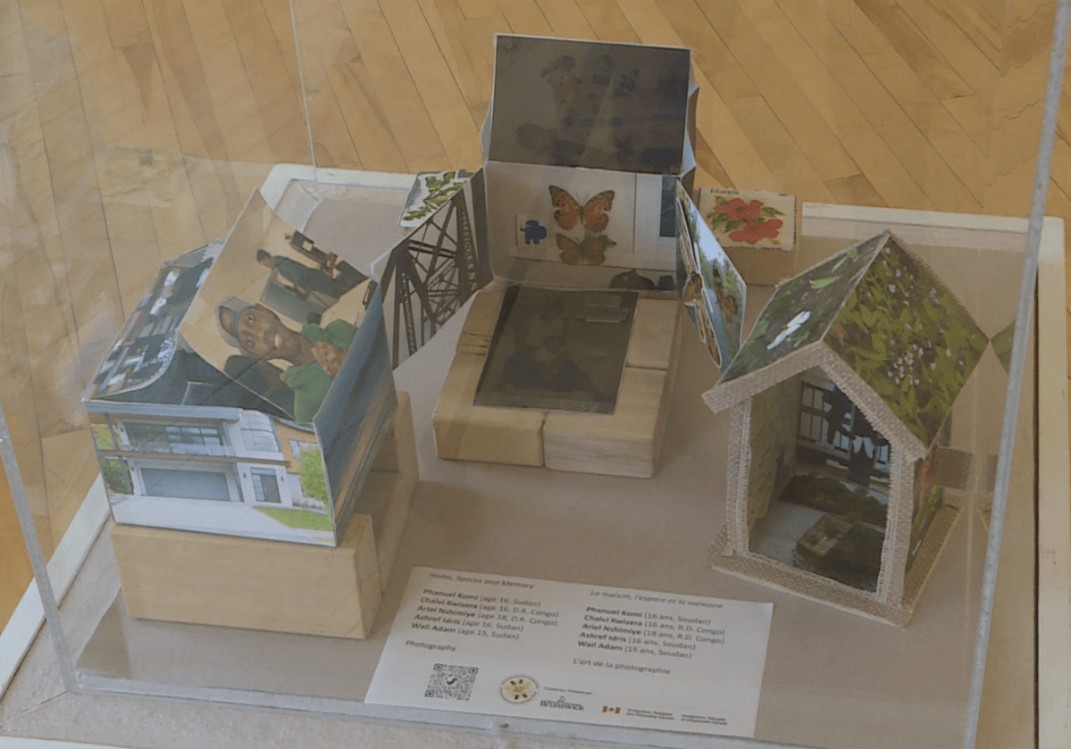 Structures that resemble houses made out of photographs are displayed in a see-through box.
