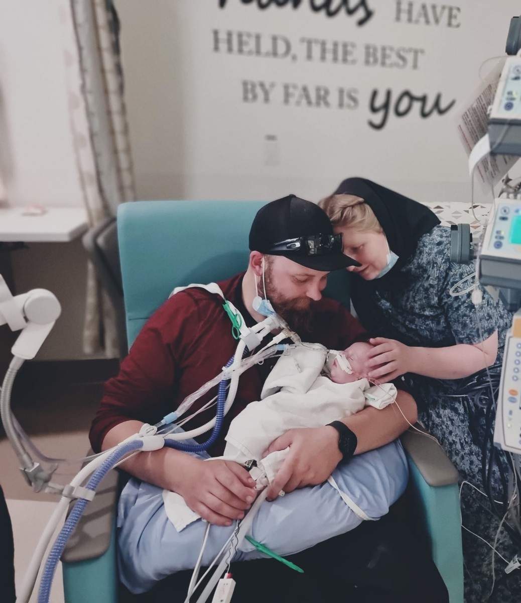 A mother and father hold their young baby in hospital