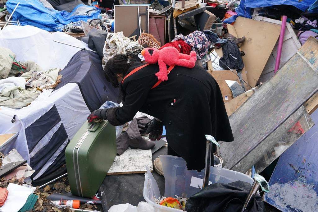 A woman looks through some belongings outside of the St. Stephen-In-The-Fields Anglican Church in Toronto as the city begins clearing out the encampment on Friday Nov. 24, 2023. New research published today says people who are homeless have high rates of COVID-19 reinfection. THE CANADIAN PRESS/Chris Young.