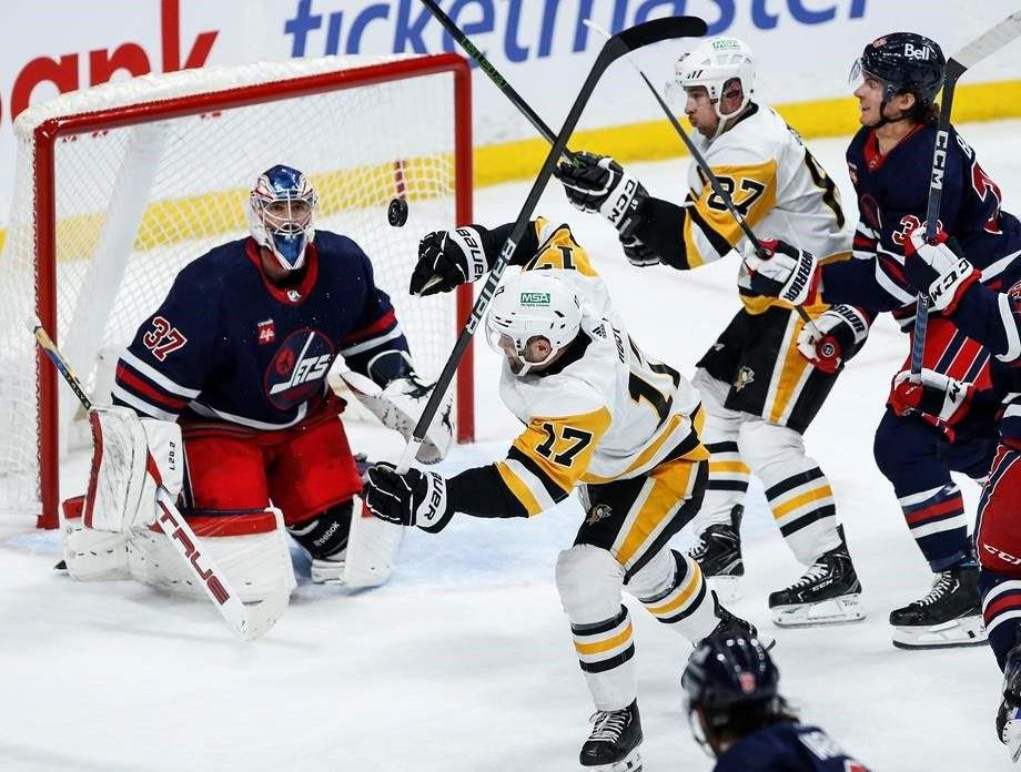 Winnipeg Jets goaltender Connor Hellebuyck (37) keeps his eye on the loose puck as Pittsburgh Penguins' Bryan Rust (17) and Sidney Crosby (87) battle Jets' Morgan Barron (36) during second-period NHL action in Winnipeg on Saturday, Feb. 10, 2024.