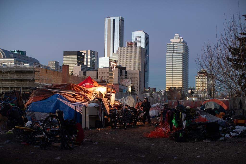 A man prepares to move his belongings as police and cleanup crews prepare to tear down homeless encampments in Edmonton on Friday, Dec. 29, 2023. Unhoused people have a fundamental right to live in encampments, and that right is violated when authorities tear them down, Canada's housing advocate says.
