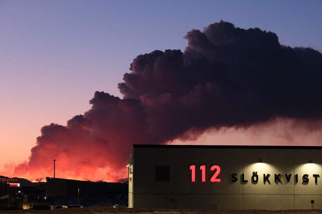 Molten lava and billowing smoke pours out of a fissure behind a fire station during a volcanic eruption near Grindavik, western Iceland on February 8, 2024.