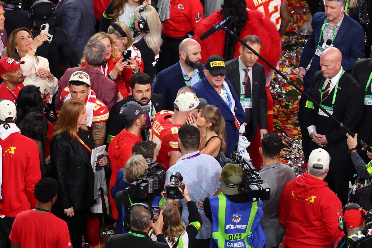 Travis Kelce and Taylor Swift kissing. There is a crowd around them.