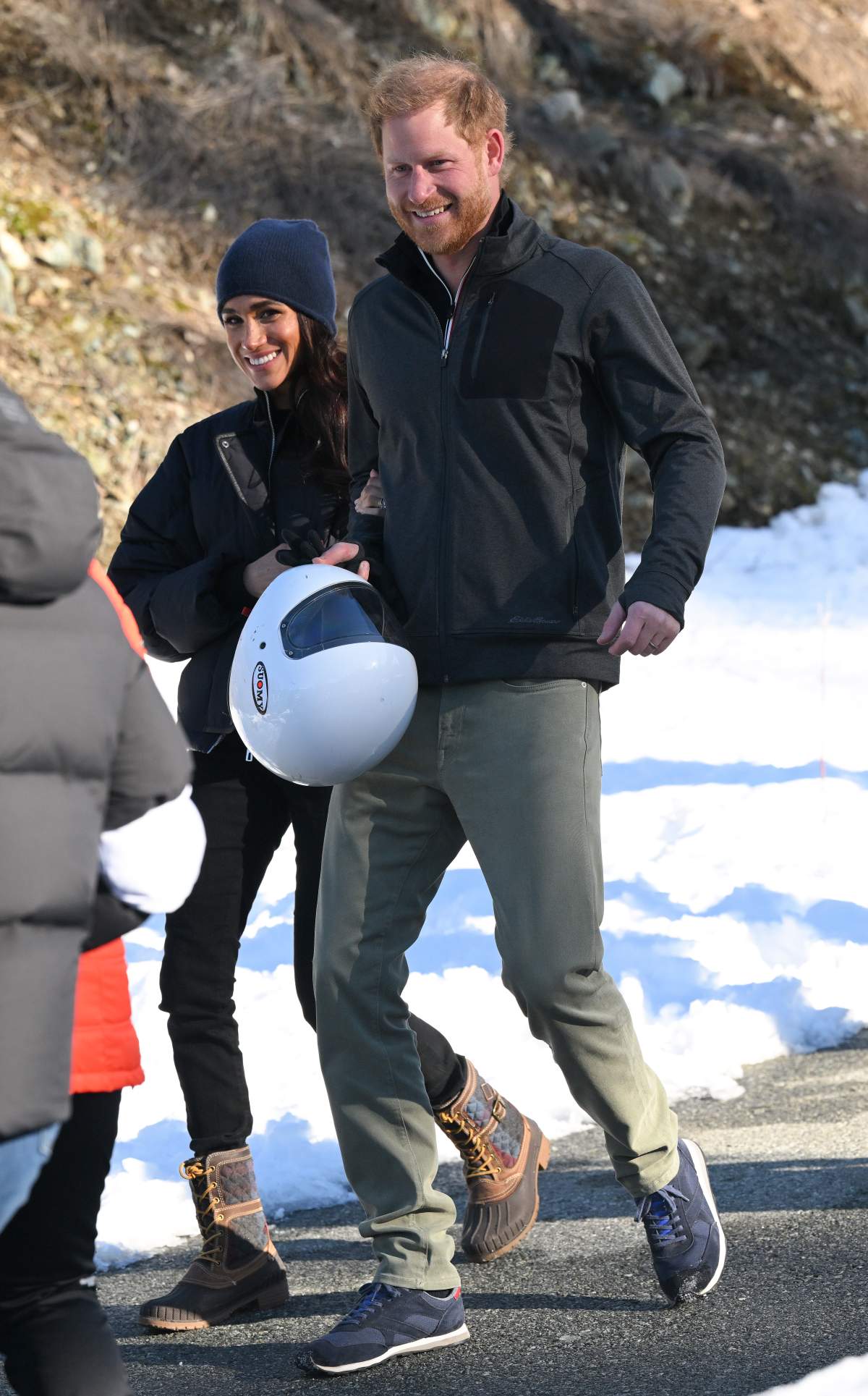 Prince Harry and Meghan Markle standing in the snow. Harry is carrying a white skeleton helmet.
