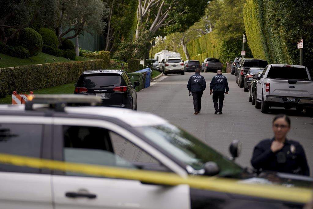 Police seen walking on a residential street. There is a police cruiser and yellow tape in the foreground,