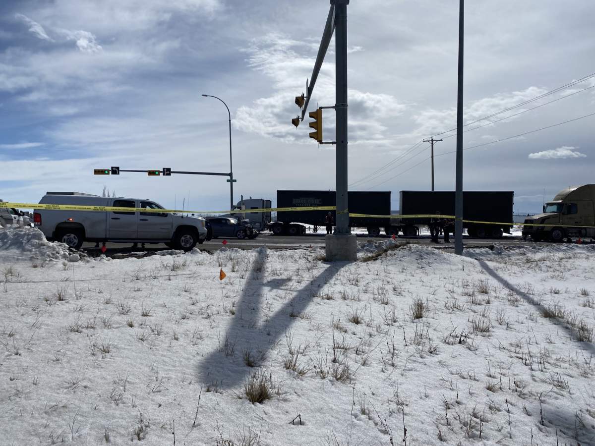 Emergency tape surrounds the scene of a collision in Calgary's southeast on March 27, 2024, with a damaged car and semi-trailer truck behind the tape.