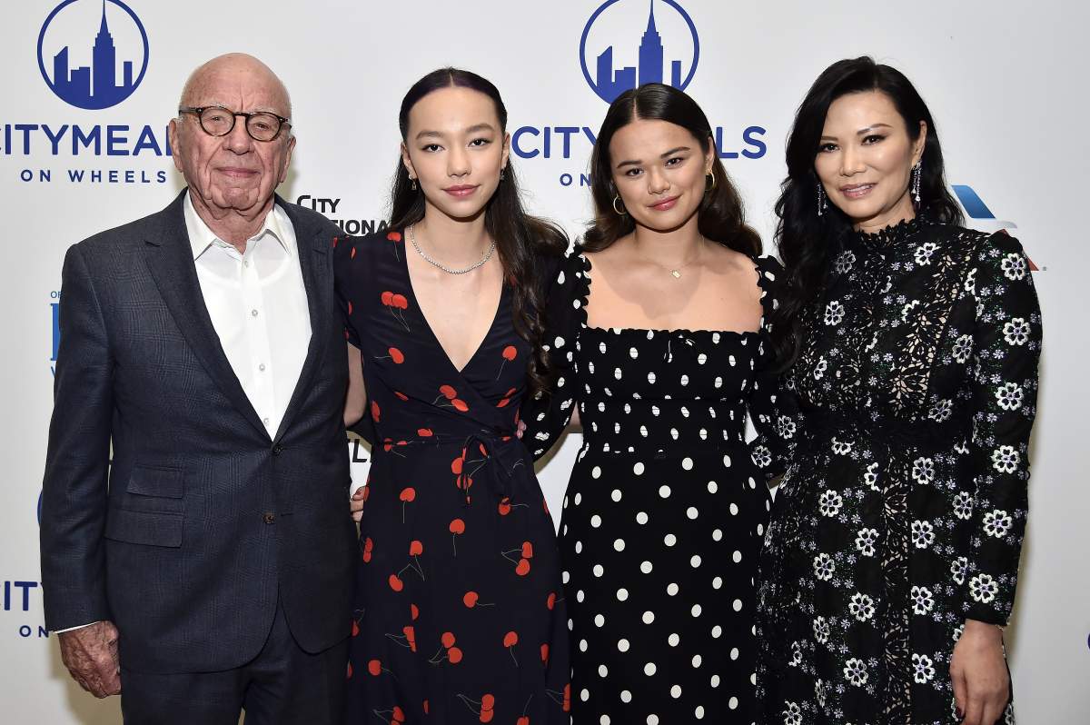 Rupert Murdoch, Grace Murdoch, Chloe Murdoch, and Wendi Deng on a red carpet. Murdoch is wearing a black suit. The three women are also wearing patterned, black dresses.