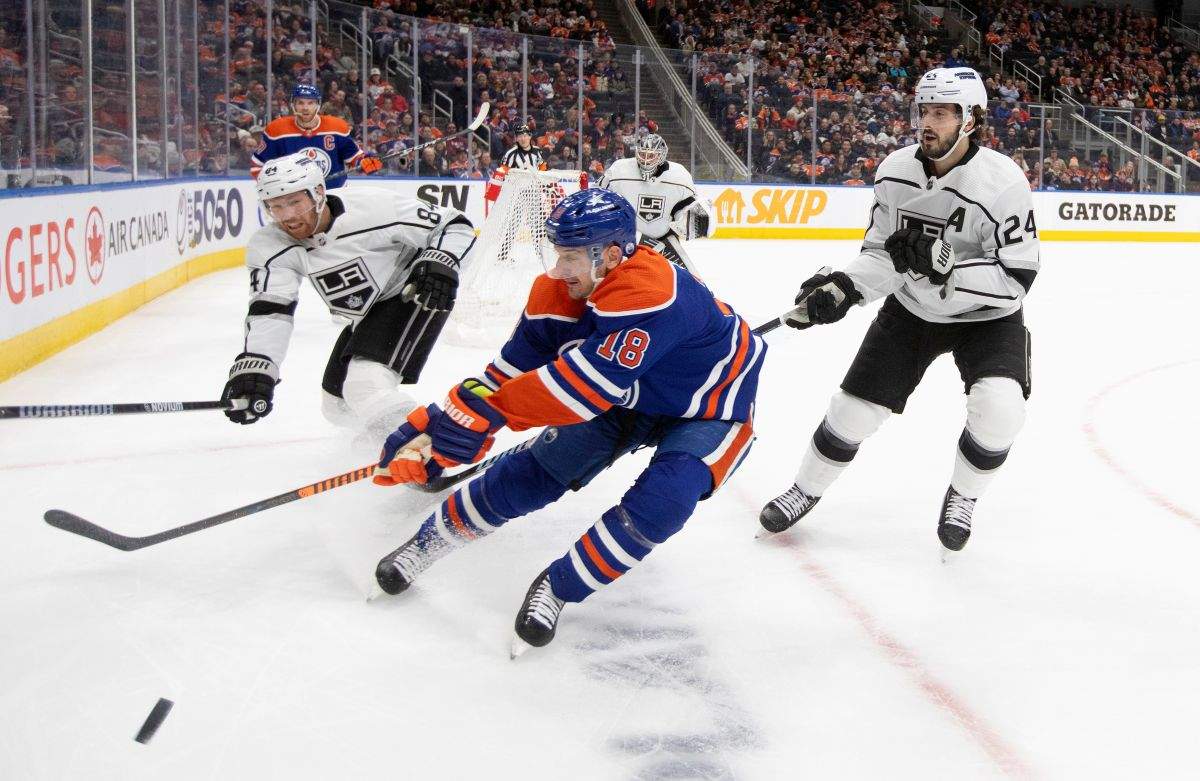 Los Angles Kings' Vladislav Gavrikov (84) and Phillip Danault (24) battle for the puck with Edmonton Oilers' Zach Hyman (18) during second period NHL action in Edmonton on Monday February 26, 2024.