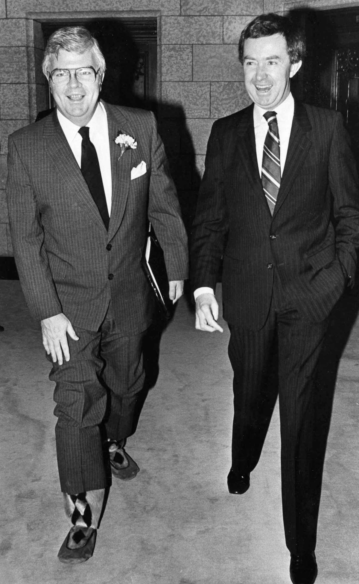 Accompanied by Prime Minister Clark as he makes his way to the Commons to deliover his first budget Dec. 11, 1979, in Ottawa. Finance Minister John Crosbie lifts his pant leg to display his new boots. Anew pair of shoes is a tradition for finance ministers on budget night.