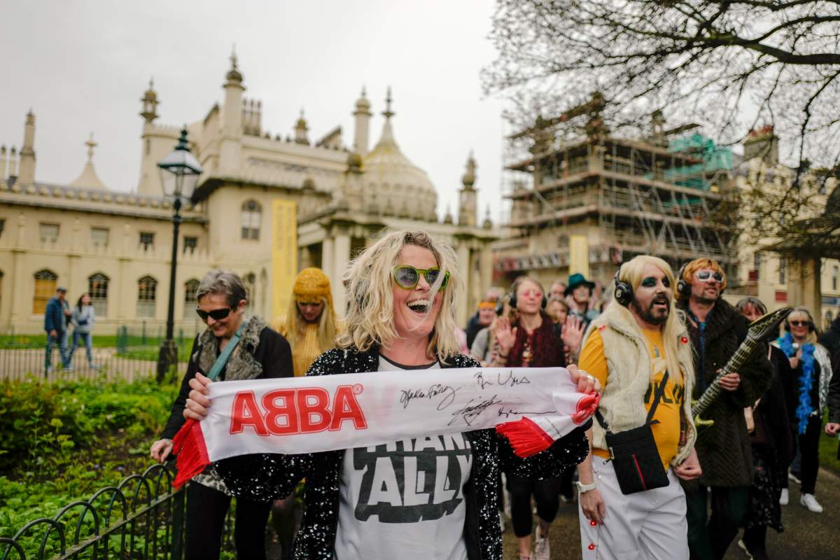 A woman holds an ABBA scarf, during a silent disco event outside the Brighton Dome, in Brighton, England, Saturday, April 6, 2024. Fans are celebrating 50 years since ABBA won its first big battle with “Waterloo.” A half century ago on Saturday, April 6, the Swedish quartet triumphed at the 1974 Eurovision Song Contest with the peppy love song.