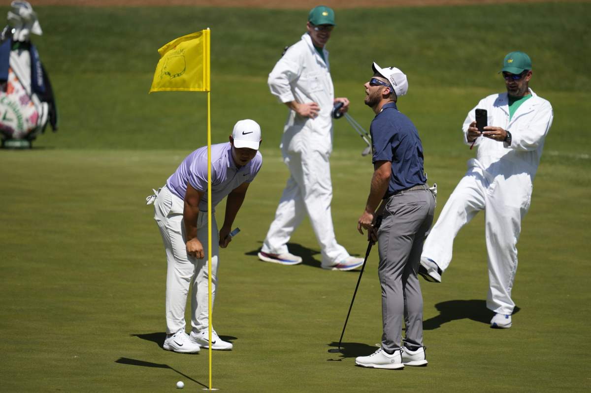 Tom Kim, left, of South Korea, watches Sam Burns putt as Burns wears solar eclipse glasses on 16th hole during a practice round in preparation for the Masters golf tournament at Augusta National Golf Club Monday, April 8, 2024, in Augusta, Ga. (AP Photo/Ashley Landis)