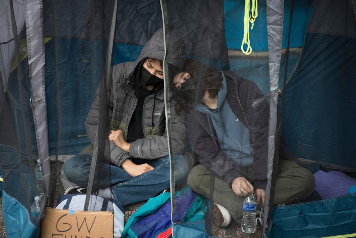 Students protesting the Israel-Hamas war at George Washington University sit in a tent to avoid the rain in Washington, Saturday, April 27, 2024.