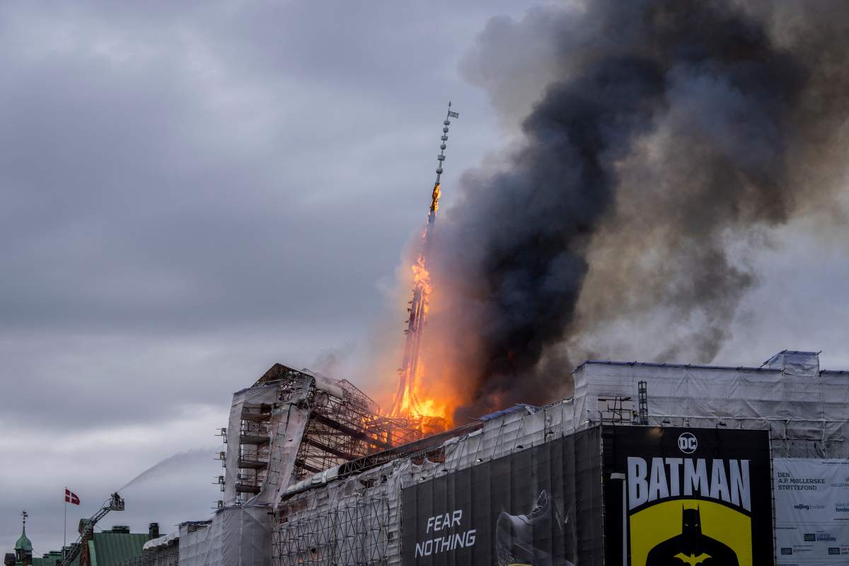 The stock exchange spire, tilted, is on fire. Dark smoke plumed.