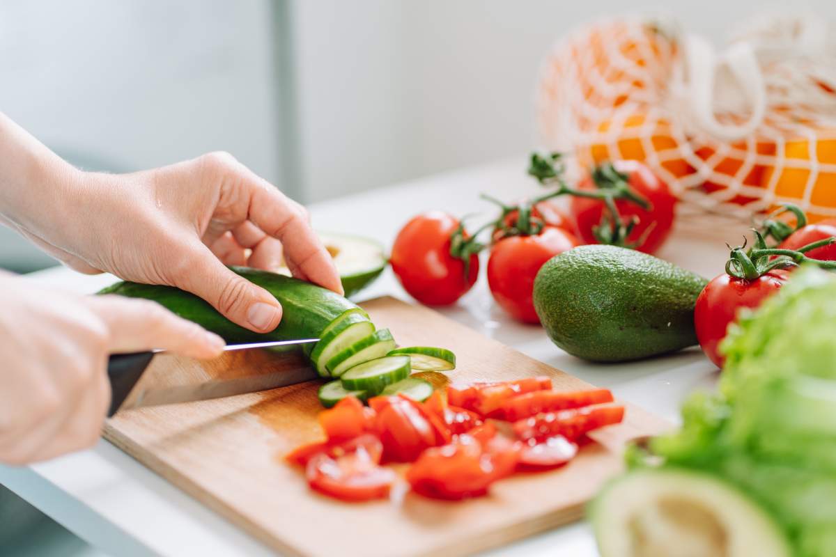 Woman preparing fresh raw organic vegetable salad on wooden board