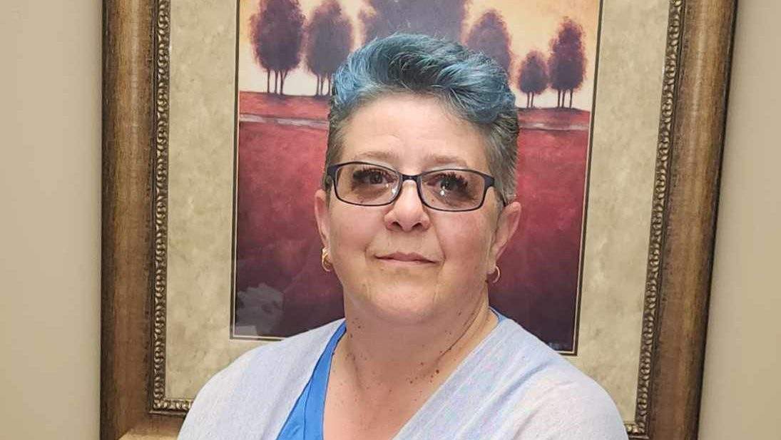 A woman with blue hair and glasses poses for a portrait.