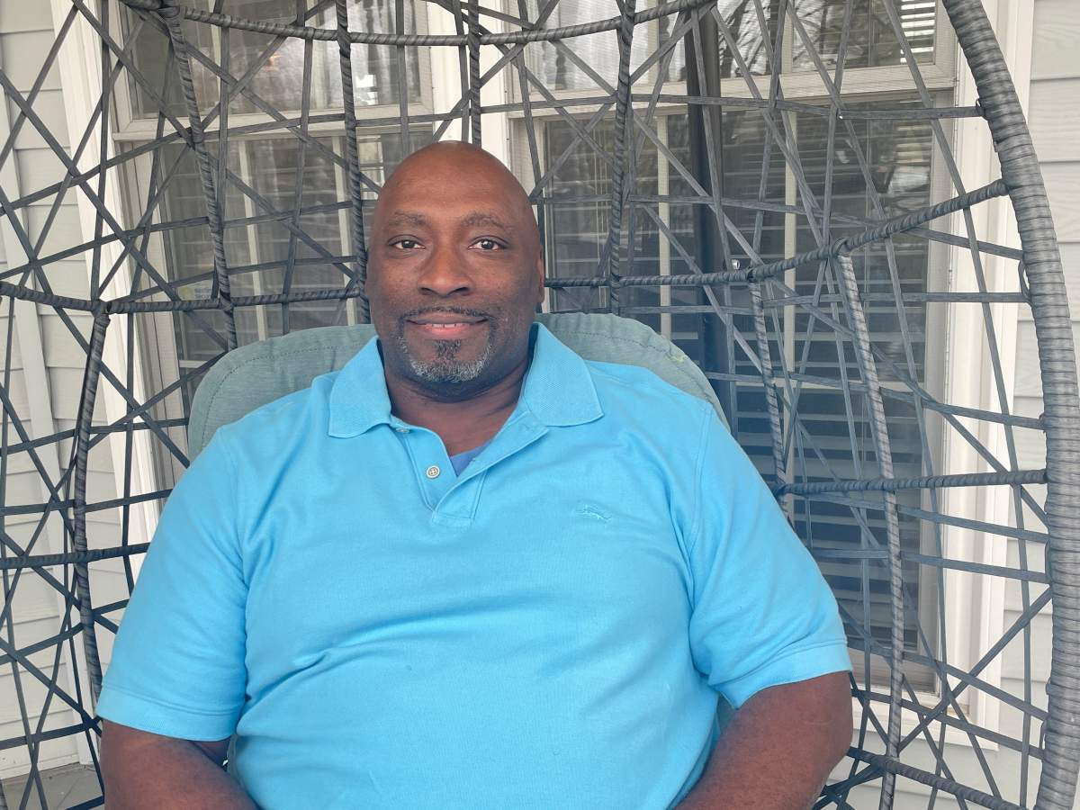 a Black man wearing a blue shirt sits in a hanging basket chair