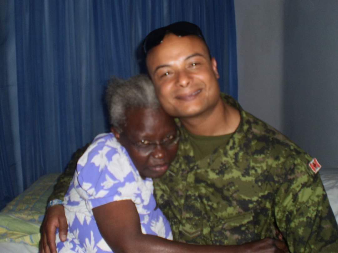 A man in combat fatigues hugs an older woman with white hair wearing a purple flowered dress