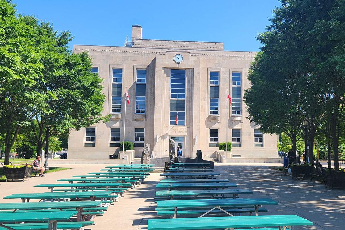 A courthouse building on a sunny day with leafy green trees and benches outside.
