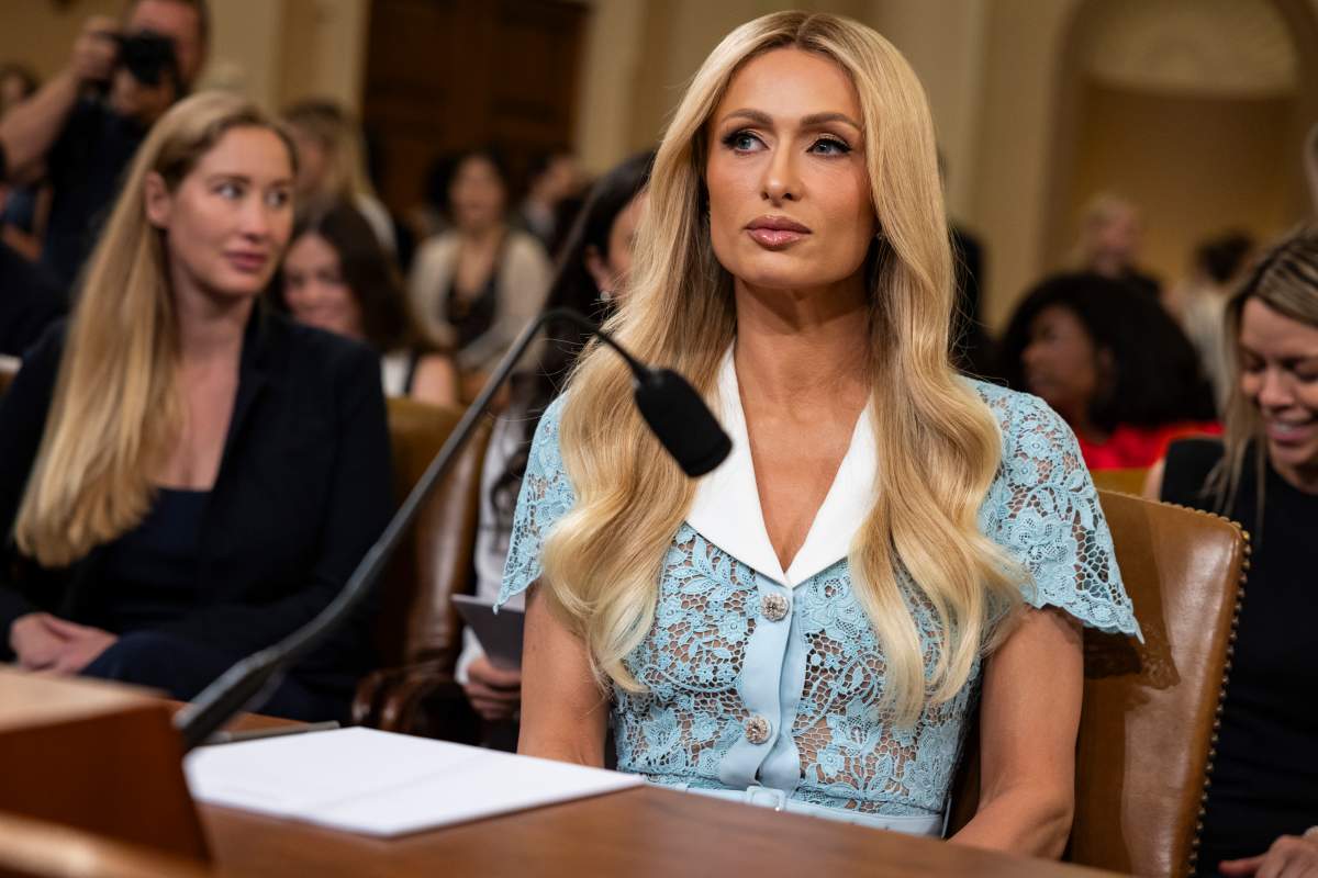 Paris Hilton sitting in front of a microphone. She is wearing a blue, lace dress with a white collar. Her blonde hair is long.
