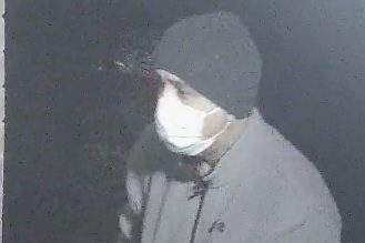 A surveillance photo of a man in a mask and dark-coloured clothing.