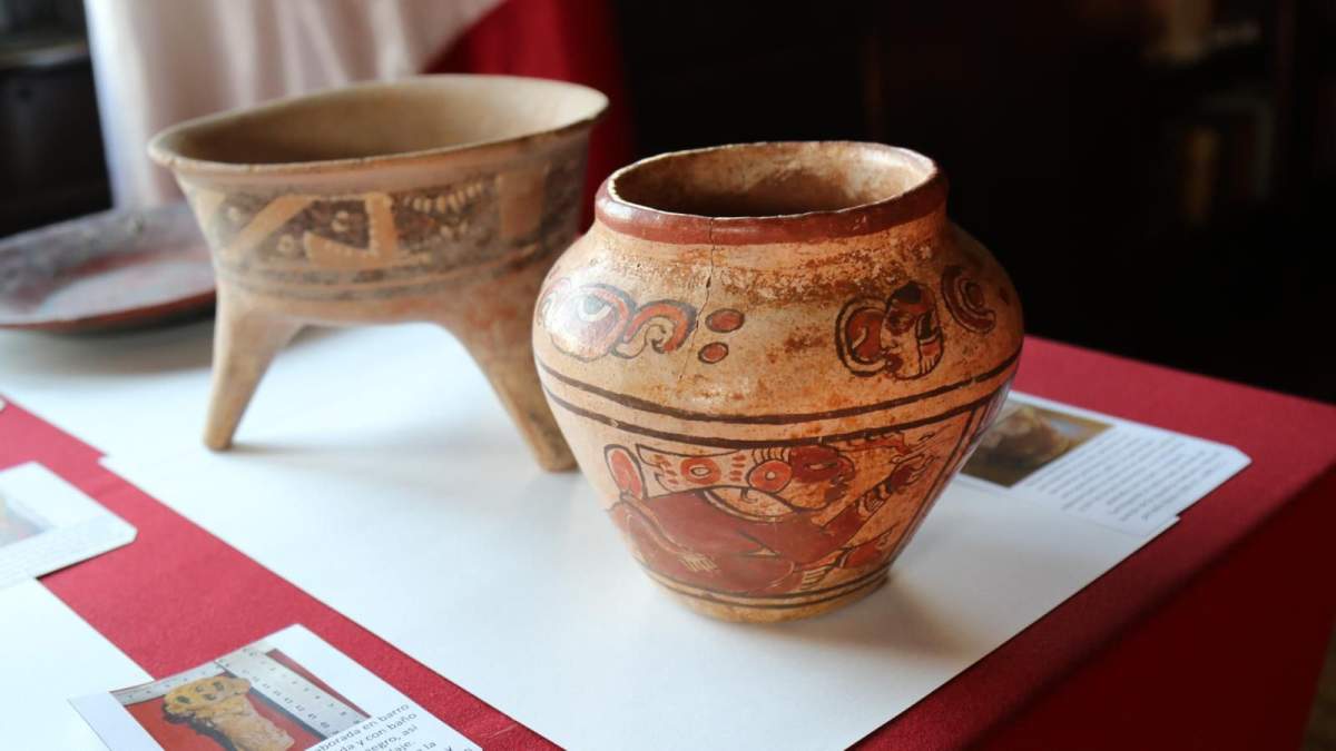 Two pieces of pottery. The vase in the front, Dozier's, is round and wide at the top, with traditional art on its side.