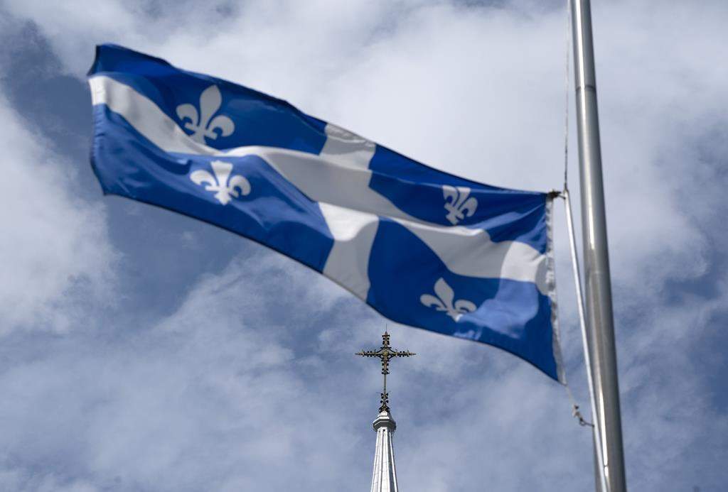 The Quebec flag flies on a flag pole near a church.