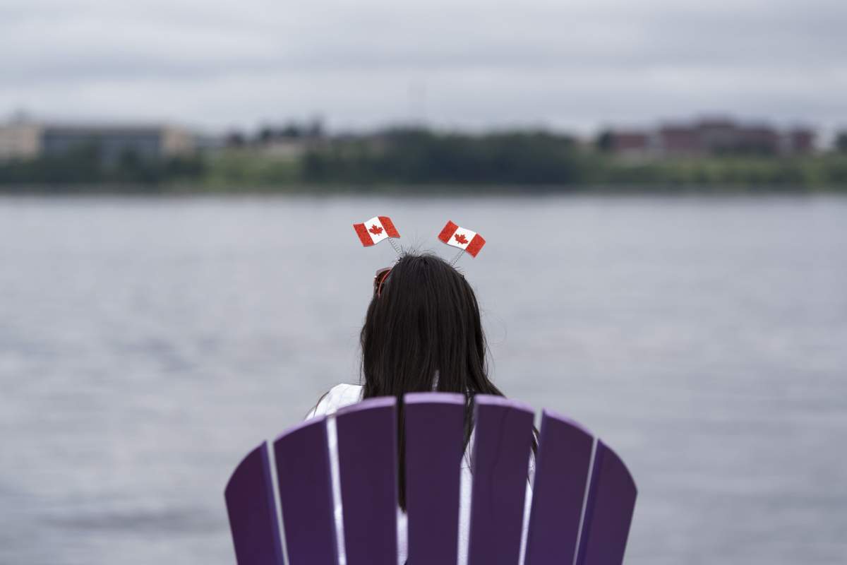 A reveller wearing a Canada flag fascinator sits in an Adirondack chair on the waterfront on Canada Day in Halifax on Monday, July 1, 2024. Due to inclement weather, a number of Canada Day celebrations were cancelled in Halifax. THE CANADIAN PRESS/Darren Calabrese