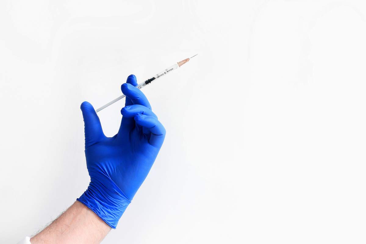 Doctor's hand in blue medical glove holding open syringe with medical solution.
