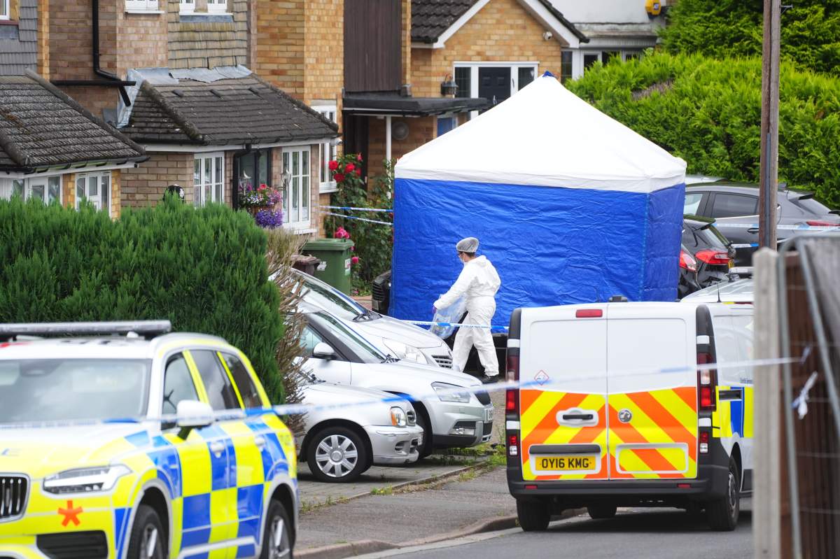 A blue tent on a British street. There are police vehicles and someone wearing a white hazmat suit.