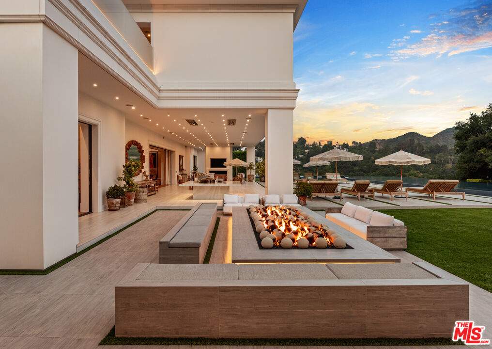 A backyard firepit next to a green lawn with lawn chairs and a pool in the background.