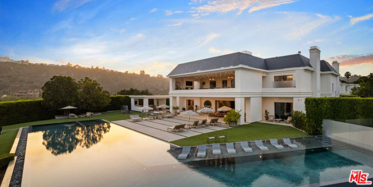 A large infinity pool wraps around the back of a mansion with lounge chairs embedded in the shallow part of the pool.