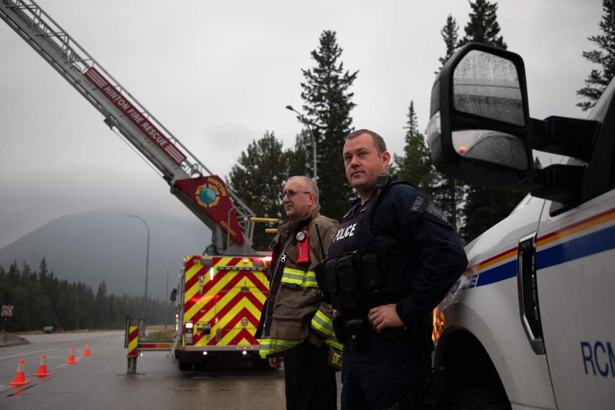 Hinton Fire Chief Mac de Beaudrap and an RCMP officer wait at the Park gate to greet returning residents to Jasper, Alberta on Friday August 16, 2024. Wildfire caused evacuations and widespread damage in the National Park and Jasper townsite.