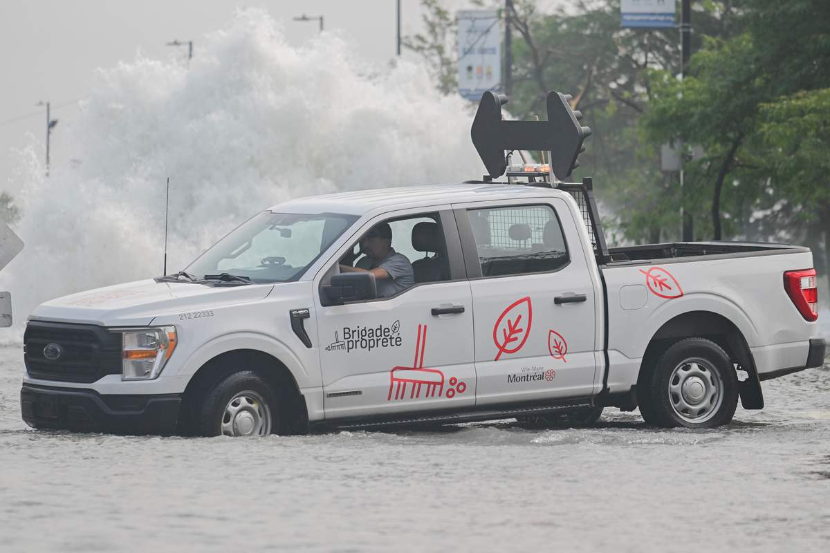 A city vehicle navigates a flooded street next to a geyser caused by a broken watermain in Montreal, Friday, August 16, 2024, causing flooding in several streets of the area.