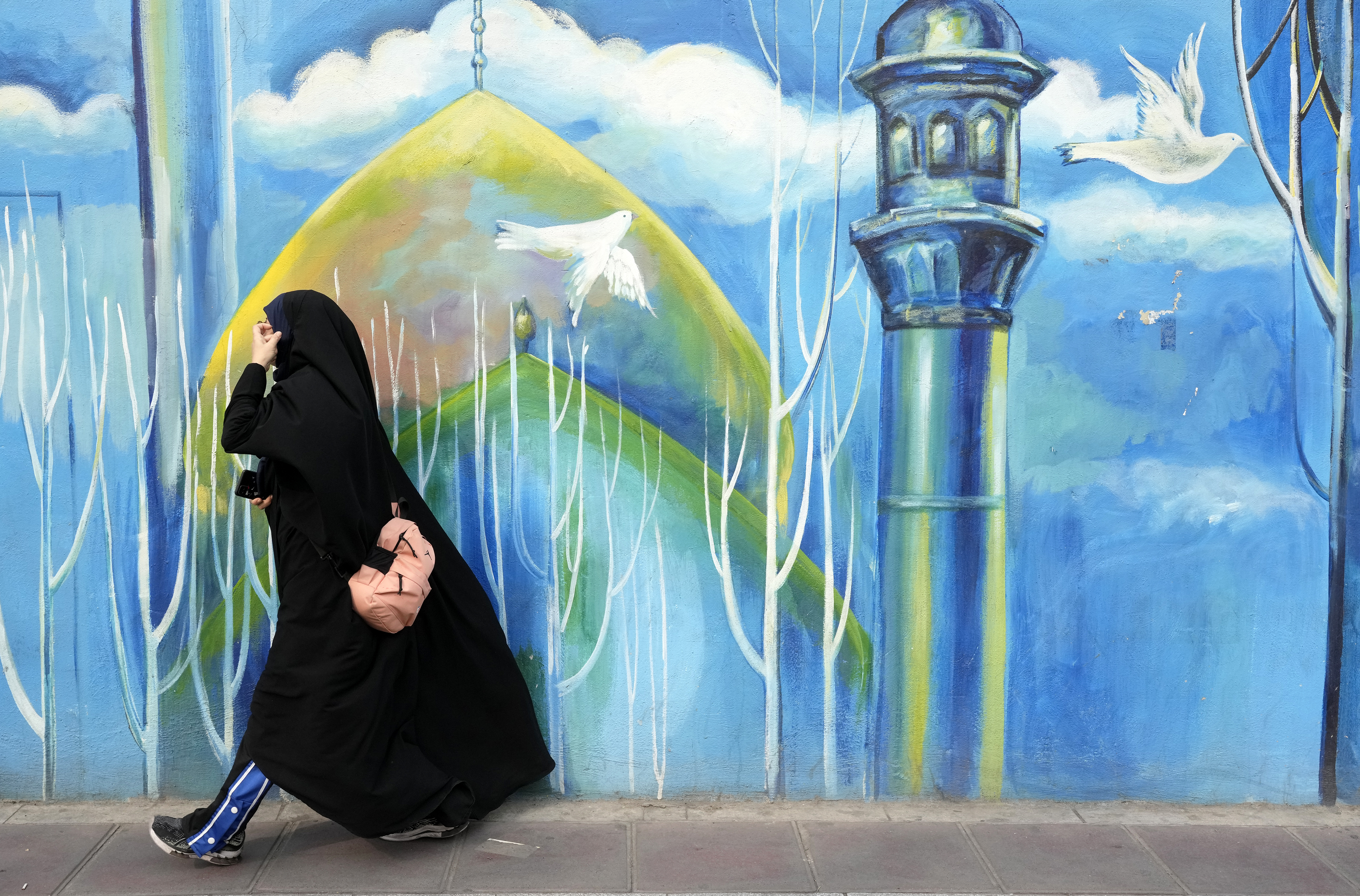 Woman walks past mural of mosque, Tehran, Iran, Feb. 22, 2024. (AP Photo/Vahid Salemi)