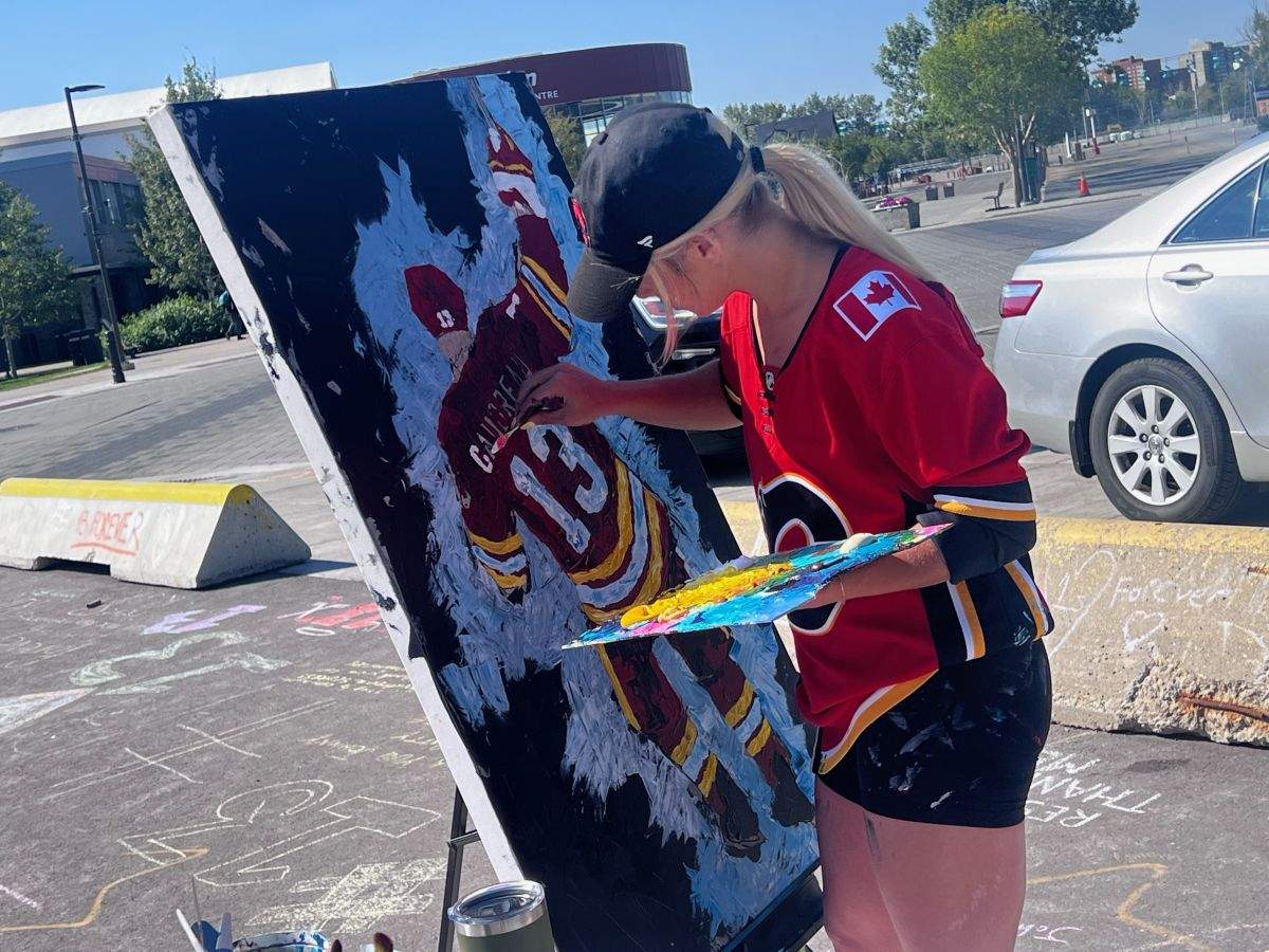 A woman works on a painting for former Calgary Flames player Johnny Gaudreau at a memorial outside the Saddledome on Sept. 3, 2024.